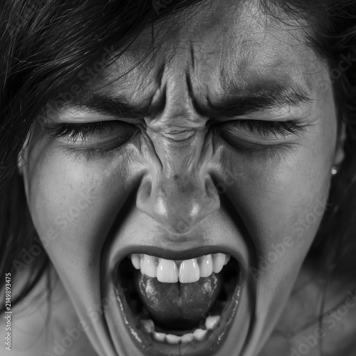 A close-up black and white photo of a woman screaming with eyes shut tight, showing intense emotion and tension.