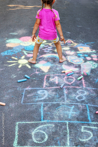 Little girl playing hopscotch drawn with chalk on asphalt