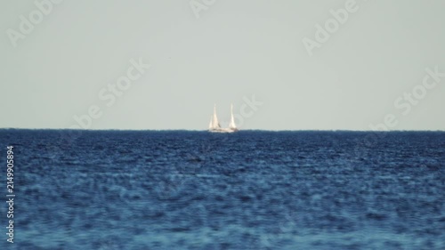 A sailing yacht far out at sea, looking like a mirage amidst warm-air distortion, in slow motion.