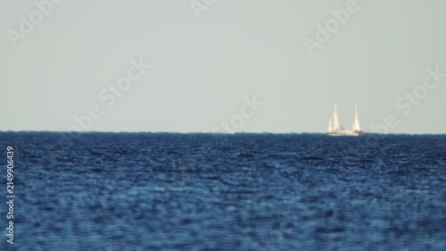 A sailing yacht far out at sea, looking like a mirage amidst warm-air distortion, in slow motion.