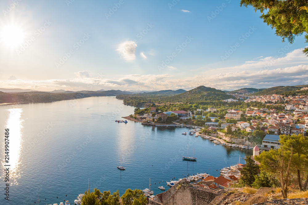 Fototapeta premium View from Saint Michael’s Fortress in Šibenik, Croatia, at sunset, overlooking charming stone houses, the sparkling Adriatic Sea, and a breathtaking coastal panorama bathed in warm golden light.