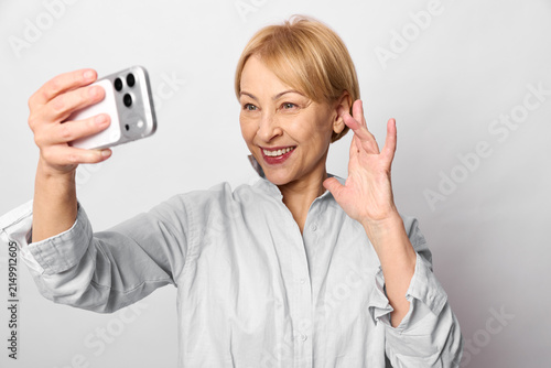 Foto Smiling senior woman takes a smartphone selfie, waving
