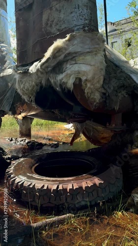 A close-up view of heavily damaged and rusted military vehicle wreckage covered in fibrous material and sitting in mud and water.
