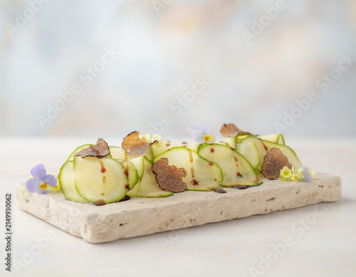 Gourmet zucchini carpaccio appetizer beautifully presented on a natural stone board, featuring fresh black truffle slices, vibrant edible flowers, and a savory balsamic drizzle