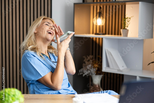 Medical worker wearing scrubs laughing while talking on a mobile phone during a break in clinic