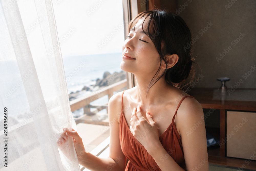 Naklejka premium 海を望む窓辺で目を閉じるオレンジ色の服の女性