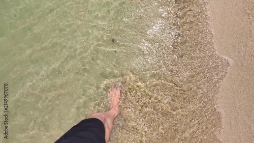 First-person view shows bare feet entering calm, shallow sea water