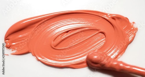 Coral-colored cosmetic cream being smeared on a white surface, thick liquid texture application, beauty and skincare product swatch.