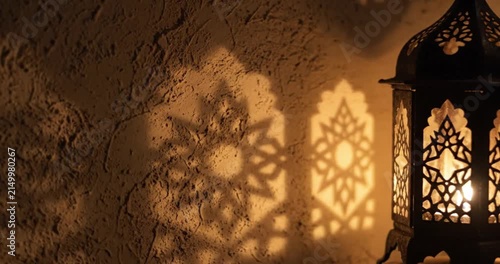Decorative metal lantern casting intricate geometric light patterns on a textured wall, warm ambient mood lighting.
