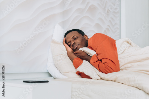 Canvastavla Young black man sleeping soundly in a comfortable bed at home, embracing healthy