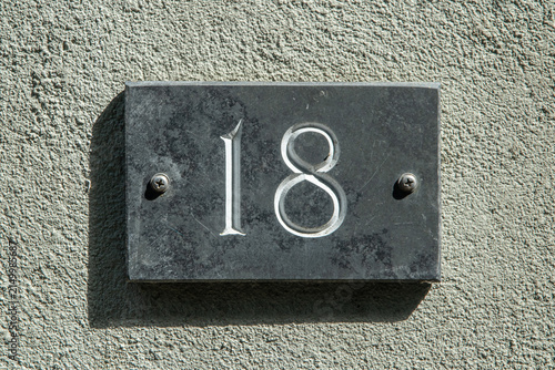Weathered house number 18 on a dark rectangular plaque mounted on a textured exterior wall.