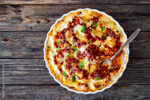 Bolognese pasta casserole - baked rigatoni noodles with bolognese sauce, mozzarella cheese and béchamel sauce on wooden table. Top view
