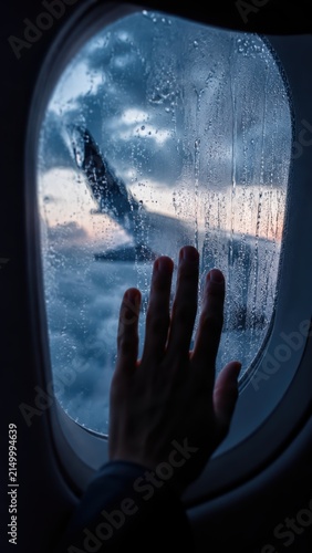 Passenger hand touching airplane window with rain drops and wing view photo