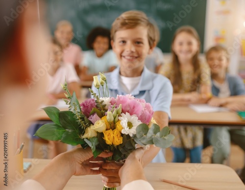 Schoolboy giving flower bouquet to teacher in classroom