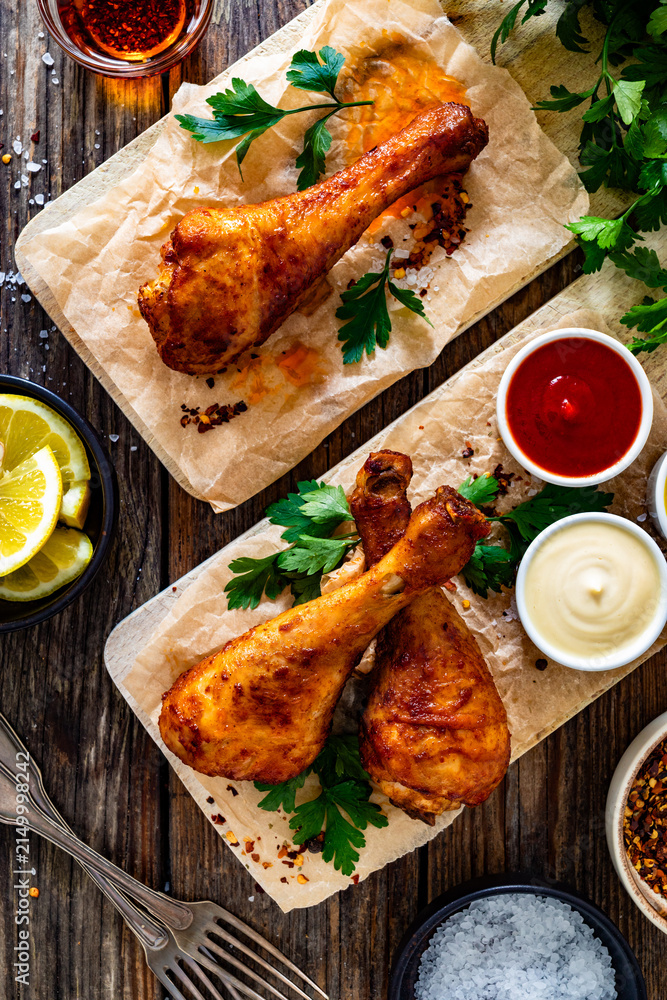 Fototapeta premium Air fryer chicken drumsticks with mayonnaise, ketchup and mustard on wooden table. Top view