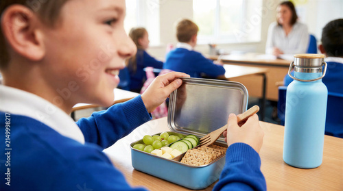 Student enjoying healthy food with stainless steel lunch box and water bottle in classroom