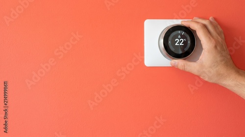 Man adjusting smart thermostat set to twenty two degrees on orange wall for heating control concept