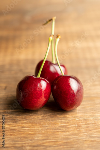 Close-up of three ripe cherries with glossy skin and green stems on rustic wooden surface, natural fruit photography