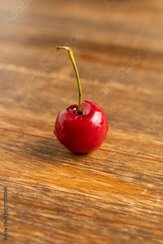 Close-up of one ripe cherries with glossy skin and green stems on rustic wooden surface, natural fruit photography