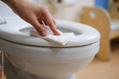 Quadro su tela Close-up of a hand wiping down a white toilet seat with a wet wipe for hygiene
