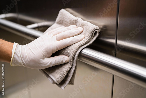 Canvas Print Close-up of gloved hand cleaning a stainless steel handrail with a microfiber cl