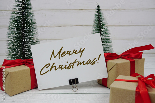 Merry Christmas! text written on paper card with gift box and christmas tree