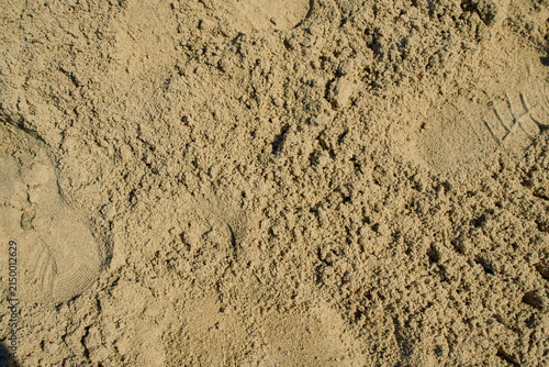 An abstract texture of yellow-brown construction aggregate sand with a shoe sole indentation