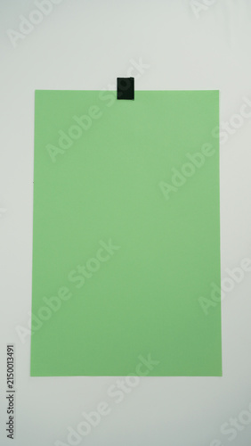Photography vertical position photo of A piece of green paper positioned vertical and attached to a surface with black tape on top, isolated on a white background