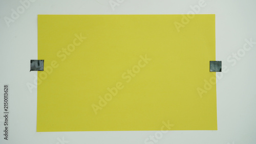Foto A piece of yellow paper positioned horizontal and attached to a surface with black tape on two sides, isolated on a white background
