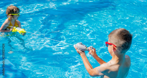 Children shooting water guns in swimming pool, water jet splash