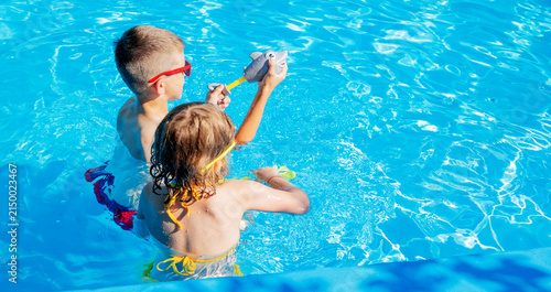 Children shooting water guns in swimming pool, water jet splash