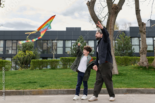 Bild auf Leinwand Handsome father and his little son enjoying a playful day in the park, flying a vibrant kite