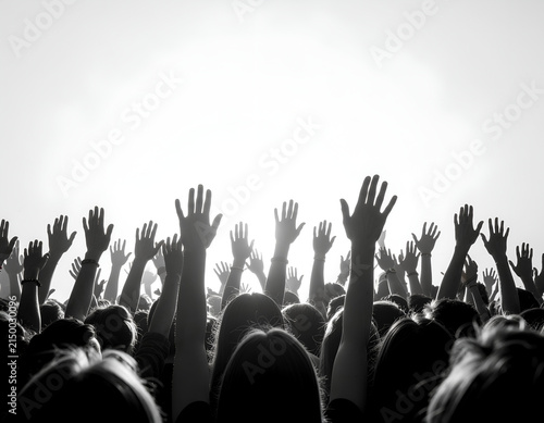A monochrome image captures a crowd of people with their arms raised towards a bright, undefined light source, conveying a sense of unity and excitement.