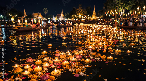 Colorful floating flowers illuminating a tranquil water surface at night during a festive celebration, surrounded by lights and city architecture