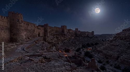 Moonlit ancient desert fortress surrounded by rugged terrain under a starry night sky, creating a mystical atmosphere