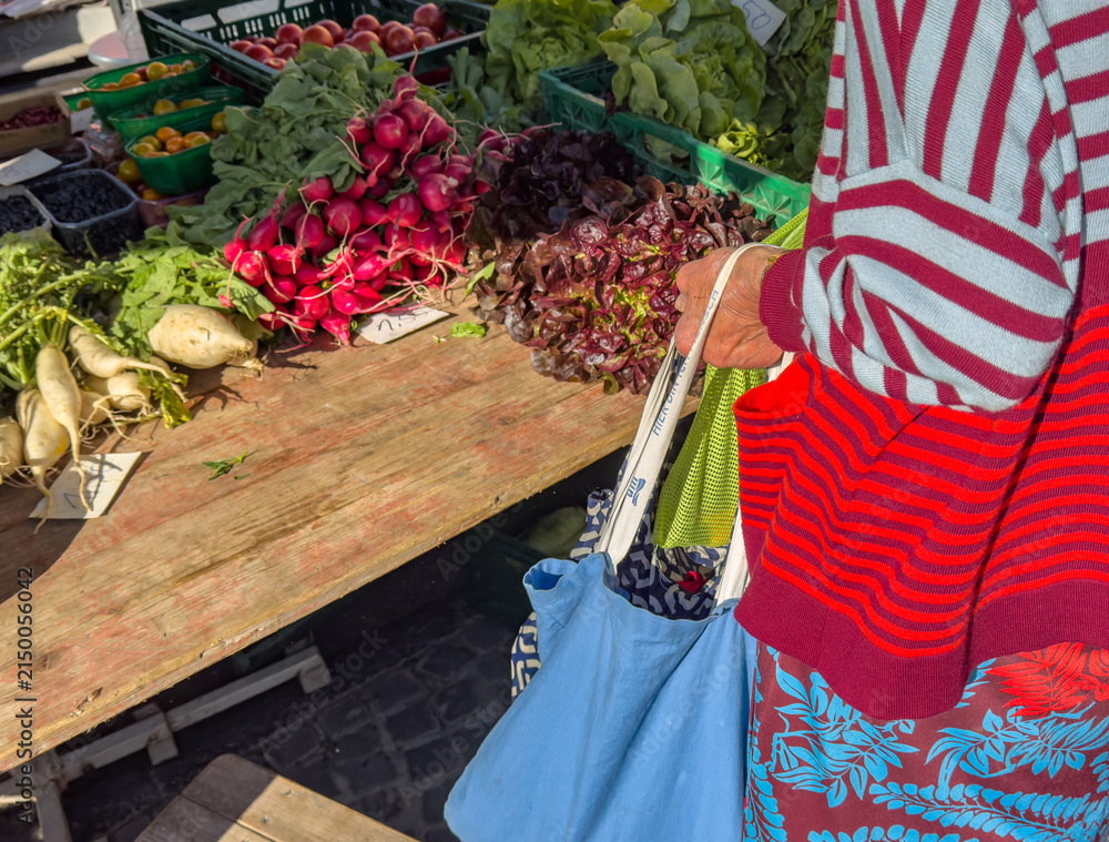 Obraz premium Older Woman Buying Fresh Organic Vegetables at a Farmers' Market in the City