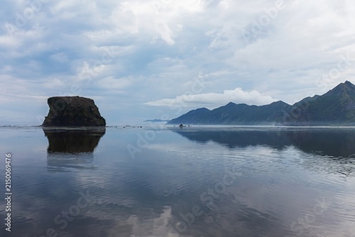 Fotografie A vast, mirror-like water surface reflects a dramatic coastal landscape, featuri