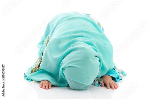 Charming young Asian Muslim child in traditional headscarf bowing down in prayer during holy month Ramadan.
