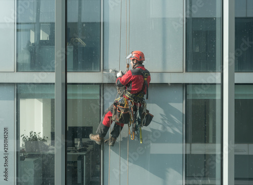 A worker climbing at height with specialized equipment is captured in a photo taken from inside a building