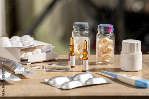 Pharmaceutical ampoules, tablets, blister packs, vials and medical supplies arranged on a wooden table. Represents medication, clinical treatment, pharmacy products and healthcare management.