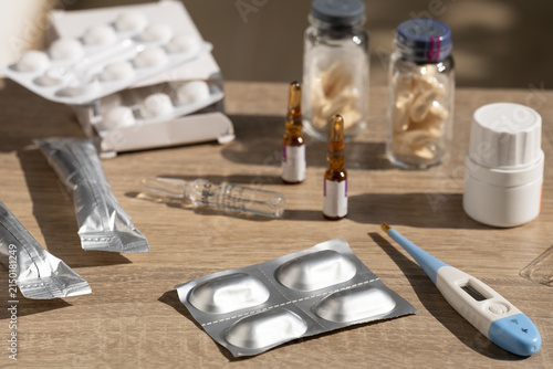 Assorted medicines and medical supplies including ampoules, tablets, blister packs, vials and a digital thermometer. Represents home healthcare, treatment, medication management and clinical care.