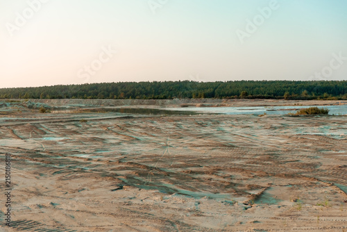 Vast sandy terrain with rippled textures and shallow water pools bordered by a dense forest.