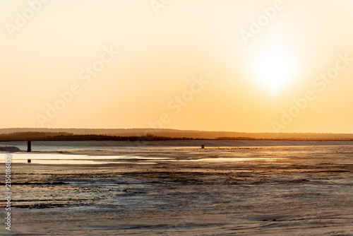 Sunset over wetlands with shallow water pools and distant forest line