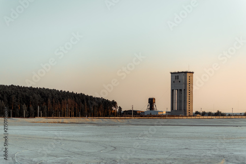 An industrial tower at a mine among a sandy area and dense pine forest