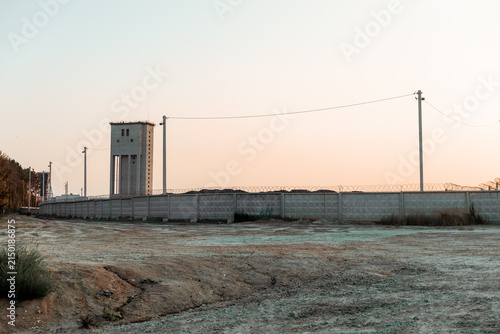 Concrete watchtower and barbed wire perimeter fence in a desolate industrial landscape