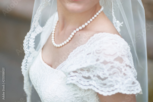 Close-up bridal portrait of a bride wearing a pearl necklace and lace wedding dress with a delicate veil, conveying elegance, romance and timeless wedding style.