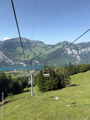 Chairlift Gondola Above a Lush Green Alpine Slope With Lake Walensee Town and Mountain Panorama in Switzerland