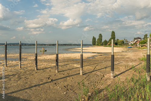Low water level at Lake Constance: Stranded boats on a dry lake bed next to a wooden jetty during a summer drought in Berlingen, Switzerland.