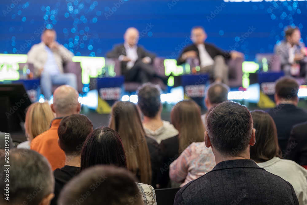 Obraz premium Attendee faces a panel of four speakers during a large business conference session.