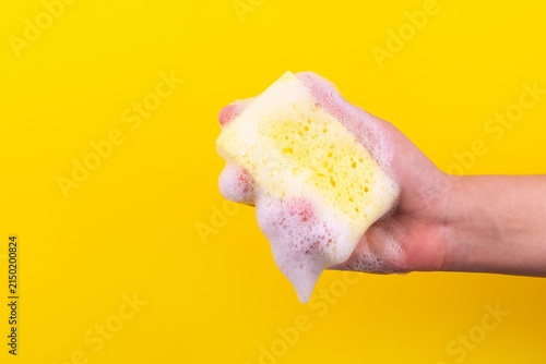 Foto Hand holding a soapy sponge against a vibrant yellow background